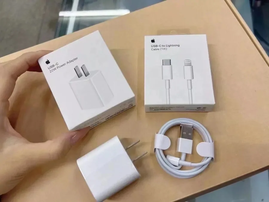 Cargador blanco de 20 vatios con cable USB-C, junto a sus cajas, sostenido en la mano