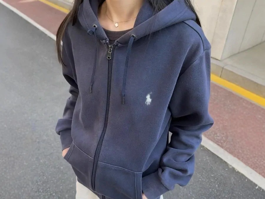 Persona con una sudadera de cremallera azul marino con capucha y un pequeño logotipo bordado, fotografiada en la calle